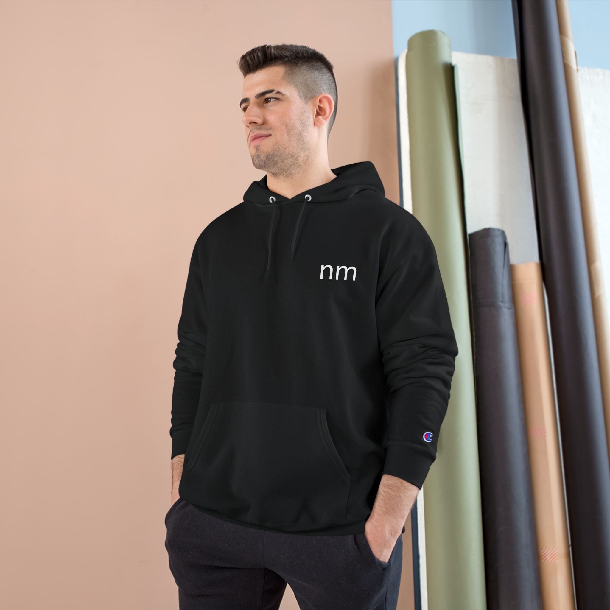 Man wearing a black hoodie with visible branding, standing against a beige wall